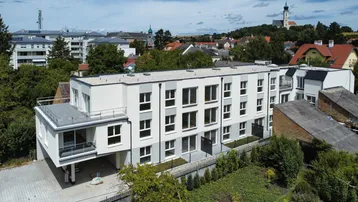 Moderne Wohnanlage mit Flachdach und umliegender Bebauung, eingebettet in eine grüne Umgebung.