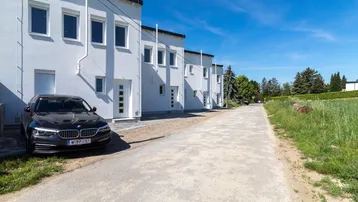 Reihe moderner weißer Reihenhäuser mit dunklem Auto davor und einer unbefestigten Straße.