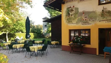 Gemütliche Außenterrasse mit Tischen und Stühlen, umgeben von Bäumen und einer bemalten Fassade.