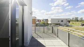 Heller Balkon mit Fliesenboden und Blick auf die umliegende Wohnsiedlung unter blauem Himmel.