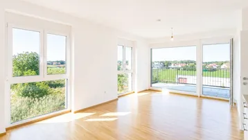 Helles, leeres Wohnzimmer mit großen Fenstern und Zugang zum Balkon, bietet weite Aussicht.