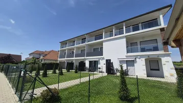 Modernes Apartmentgebäude mit mehreren Balkonen und gepflegter Rasenfläche unter blauem Himmel.