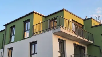 Moderne Fassade eines Wohngebäudes mit grünen und weißen Akzenten sowie mehreren Balkonen.