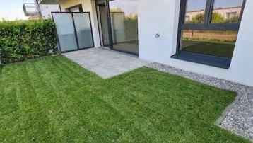 Kleiner privater Gartenbereich mit Rasenfläche und gepflasterter Terrasse vor dem Gebäude.