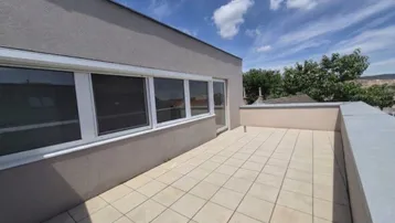 Geräumige Dachterrasse mit hellen Fliesen und Zugang zu den Innenräumen unter blauem Himmel.