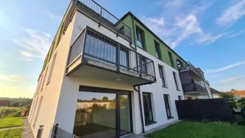 Modernes Mehrfamilienhaus mit weißer Fassade, grünen Akzenten und mehreren Balkonen unter blauem Himmel.