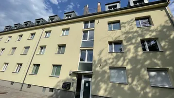 Mehrfamilienhaus mit gelber Fassade, vielen Fenstern und Dachgauben unter blauem Himmel.