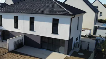 Moderne Doppelhaushälfte im Neubaugebiet mit kleiner Terrasse und unfertigem Gartenbereich.