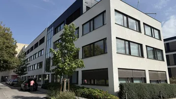 Modernes Bürogebäude mit heller Fassade und großen Fenstern unter blauem Himmel.