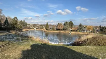 Malerischer Blick auf einen teilweise zugefrorenen See, umgeben von Bäumen und ländlicher Bebauung.