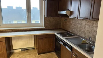 Funktionale Küche mit braunen Holzschränken, hellem Vinylboden und einem Fenster mit Blick auf die Umgebung.