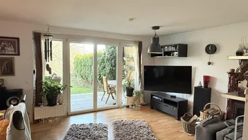 Helles Wohnzimmer mit Parkettboden, Zugang zur Terrasse und Blick in den Garten.