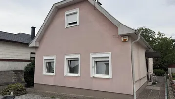 Einfamilienhaus mit rosafarbener Fassade, weißen Fenstern und Satteldach.