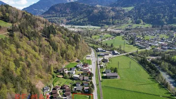 Luftaufnahme eines grünen Grundstücks mit umliegenden Häusern und beeindruckendem Bergpanorama.