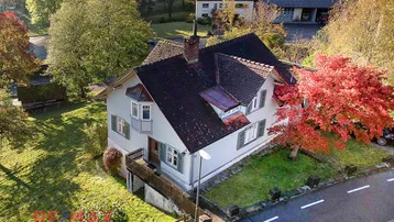 Luftaufnahme eines Einfamilienhauses mit rotem Herbstbaum und umliegender Natur.