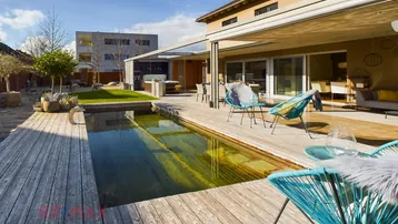Großzügiger Außenbereich mit Holzdeck, Naturpool und modernen Sitzgelegenheiten unter blauem Himmel.
