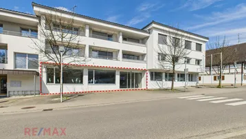 Außenansicht eines modernen Geschäftsgebäudes mit großen Schaufenstern und einer roten Umrandung.