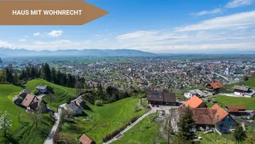 Panoramablick auf die ländliche Umgebung mit mehreren Häusern und einer Stadt im Hintergrund.
