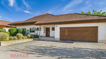 Vorderansicht des Hauses mit gepflasterter Einfahrt und integrierter Garage unter blauem Himmel.