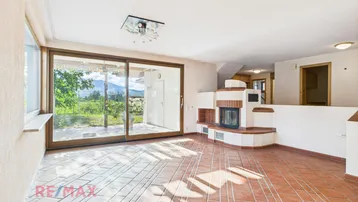 Geräumiges Wohnzimmer mit Kamin, großen Schiebetüren und Blick ins Grüne.