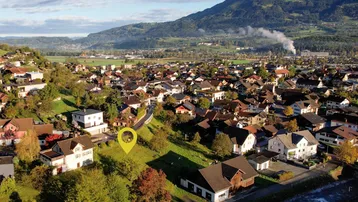 Luftaufnahme eines Wohngebiets mit Bergen im Hintergrund und markiertem Grundstück.