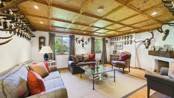 Geräumiges Wohnzimmer im alpinen Stil mit Holzkassettendecke, Kamin und Jagdtrophäen.