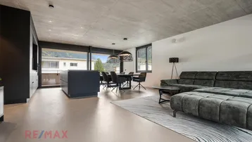 Modernes offenes Wohnzimmer mit Essbereich, Küche und Bergblick durch große Fenster.