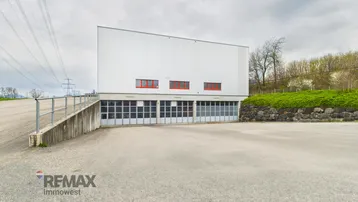 Modernes Industriegebäude mit mehreren Garagentoren und einer Zufahrtsrampe unter bewölktem Himmel.