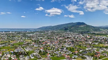 Weitläufige Luftaufnahme einer Stadt am Seeufer mit Bergen im Hintergrund unter blauem Himmel.