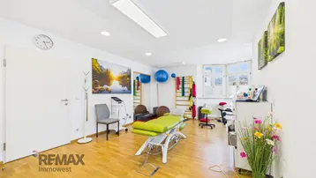 Heller Therapieraum mit Holzboden, Behandlungsliege und großen Fenstern, ideal für medizinische Praxen.