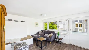 Helles Wohnzimmer mit gemütlichem Sofa, Holzboden und Zugang zum Außenbereich.