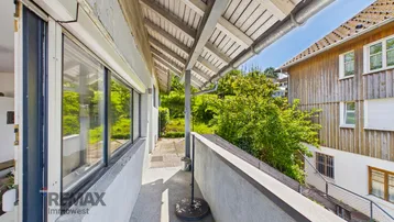 Überdachter Balkon mit Betonboden und Blick auf die grüne Umgebung und Nachbarhäuser.