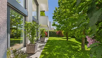 Gepflegter Gartenbereich mit Rasenfläche und modernen Pflanzkübeln neben der Hausfassade.