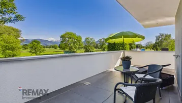 Heller Balkon mit Sitzgelegenheiten, Sonnenschirm und Panoramablick auf die Berge und Natur.