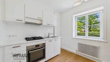Helle Küche mit weißen Schränken, Gasherd und Blick ins Grüne durch das Fenster.