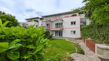 Moderne Wohnanlage mit weißer Fassade, Balkonen und gepflegtem Gartenbereich im Vordergrund.
