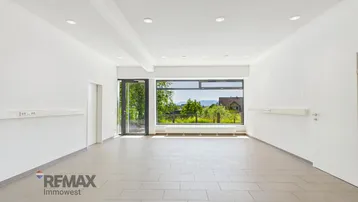 Heller, leerer Geschäftsraum mit großen Fenstern und Blick ins Grüne, ausgestattet mit Einbaustrahlern und Fliesenboden.