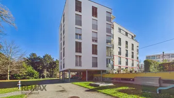 Moderne Wohnanlage mit weißer Fassade, Balkonen und umliegenden Grünflächen unter blauem Himmel.