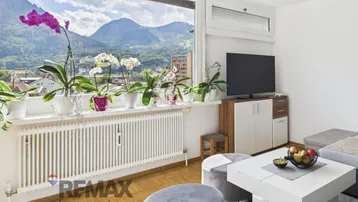 Helles Wohnzimmer mit großem Fenster, Bergblick und gemütlicher Sitzecke.