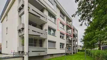 Außenansicht eines Mehrfamilienhauses mit Balkonen und Grünfläche, der Balkon der Wohnung ist markiert.