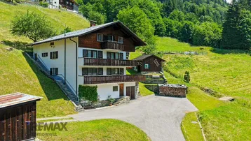 Traditionelles Haus mit Holzbalkonen und grüner Umgebung in den Bergen.