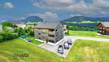 Luftaufnahme eines modernen Holzhauses mit Satteldach und Parkplätzen in ländlicher Umgebung.