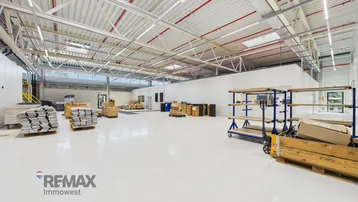 Geräumige und helle Lagerhalle mit hohen Decken, weißem Boden und sichtbaren Installationen, bereit zur Nutzung.