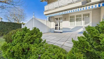 Große gepflasterte Terrasse mit direktem Zugang zum Haus und umgebender Bepflanzung.