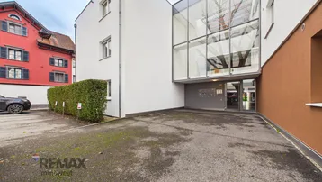 Moderne Wohnanlage mit Glasfassade, Eingangsbereich und Parkplätzen.