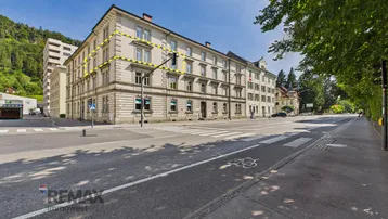 Historisches Mehrfamilienhaus mit klassischer Fassade an einer belebten Straße, umgeben von städtischer Architektur.