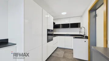 Moderne Küche mit weißen Hochglanzfronten, schwarzen Arbeitsplatten und integrierten Geräten.