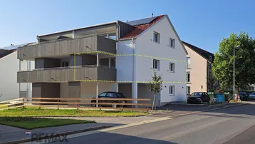 Modernes Mehrfamilienhaus mit Balkonen, Solaranlage und Parkplätzen im Freien unter blauem Himmel.