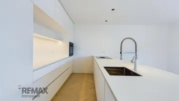 Moderne, helle Küche mit weißer Kücheninsel, integriertem Backofen und Fischgrätparkett.