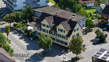 Luftaufnahme eines traditionellen Gasthofs mit gelber Fassade, umgeben von Bäumen und Straßen.